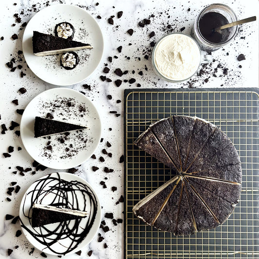 Indulgent 10 inch handcrafted cookies and cream cheesecake topped with delicious chocolate cookie crumbles, and three individually plated slices with more crumbles, homemade whipped cream and chocolate syrup