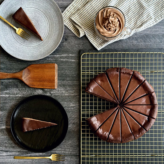 Perfectly sliced 10 inch handcrafted Triple Chocolate cheesecake, two individually plated slices of rich triple chocolate cheesecake, and a small bowl of fluffy chocolate whipped cream on the side