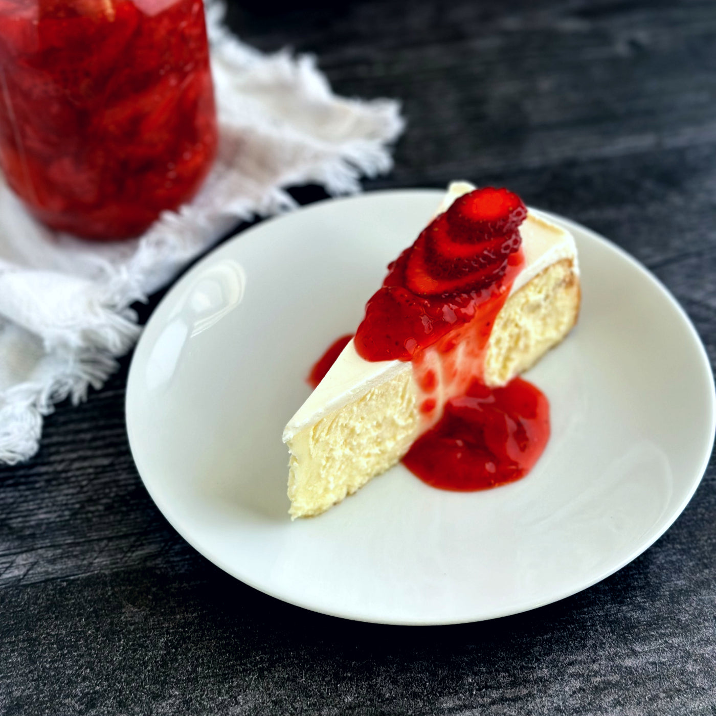 Velvety slice of Classic Cheesecake elegantly topped with a vibrant strawberry sauce delicately dripping down the sides and garnished with fresh strawberry slices