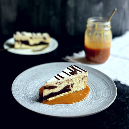 Velvety slice of Marble Brownie Swirl Cheesecake with layers of rich brownie batter baked-in,  sitting on a bed of golden homemade caramel