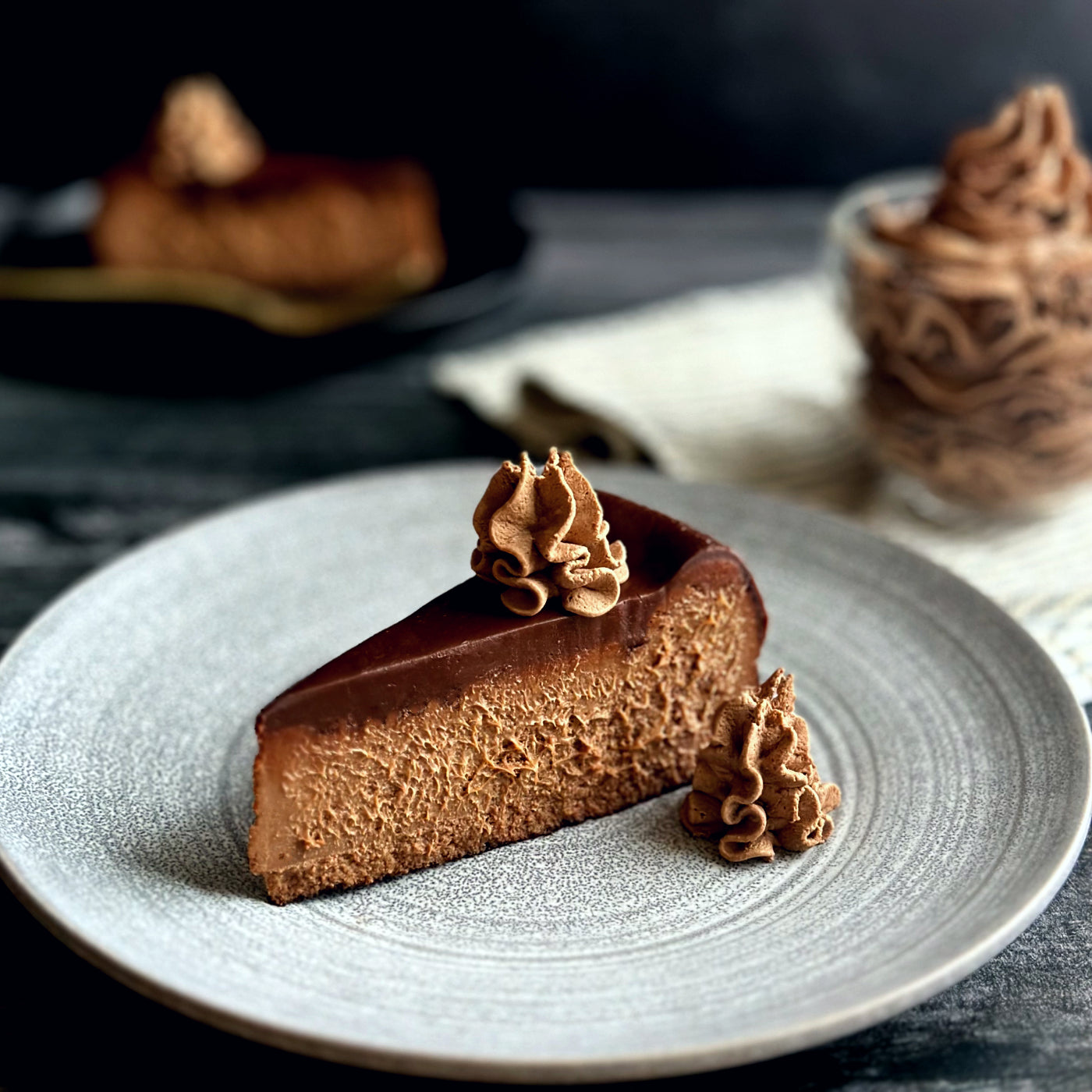 Velvety slice of chocolate cheesecake topped with a smooth layer of rich chocolate ganache and an elegant swirl of homemade chocolate whipped cream 