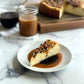 Velvety slice for Turtle Cheesecake topped with Texas Pecans, golden caramel and rich chocolate chips, sitting on an elegant combination of homemade caramel and chocolate sauces