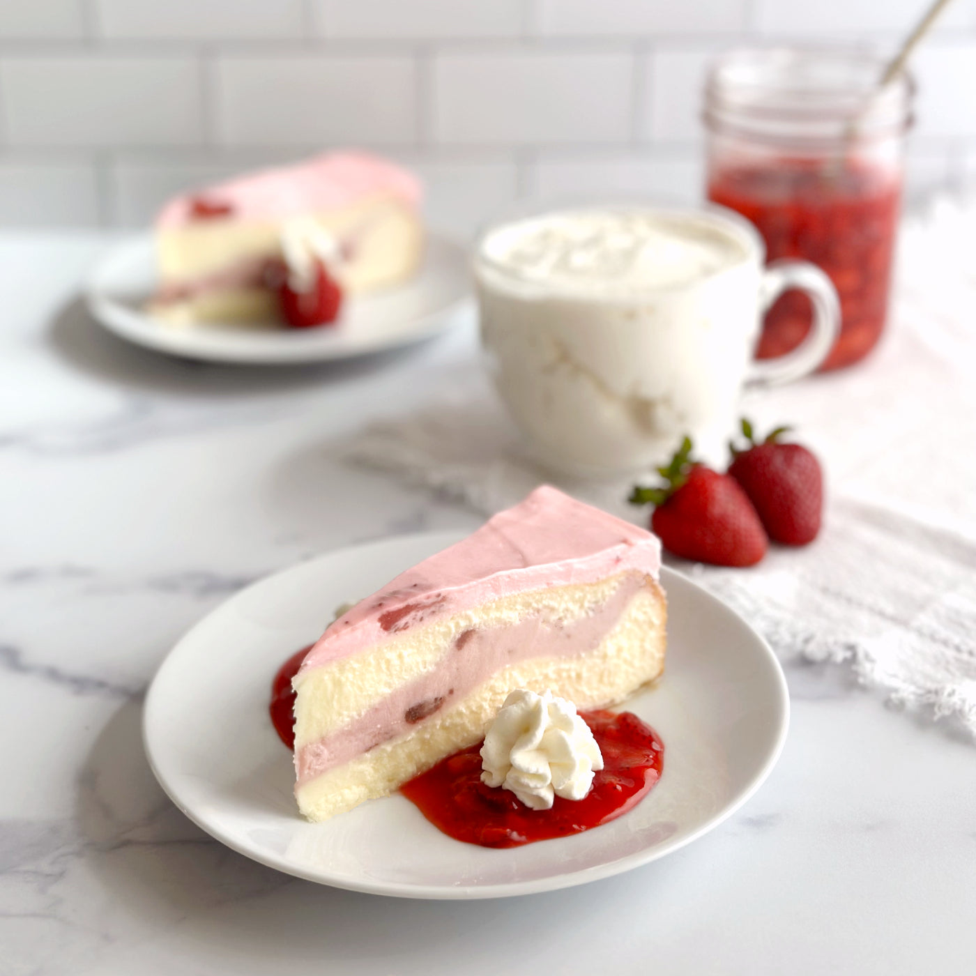 Velvety slice of Strawberry cheesecake on a bed of vibrant homemade strawberry sauce and a serving of whipped cream