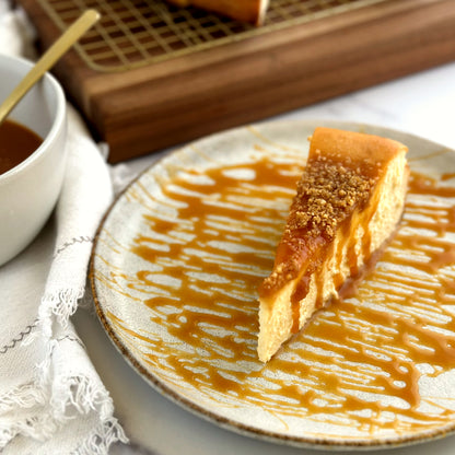 Velvety slice of Salted Caramel Cheesecake with a layer of salted caramel and cookie crumbles on top and extra homemade salted caramel drizzled over the slice and plate