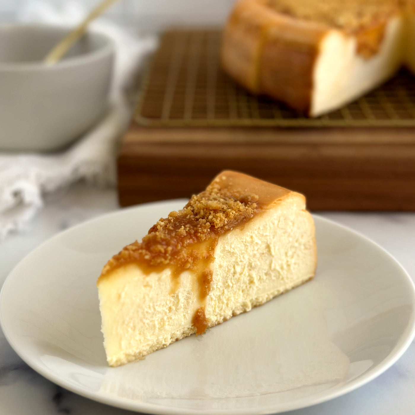 Velvety slice of Salted Caramel Cheesecake with a layer of salted caramel and cookie crumbles on top and dripping over the side.